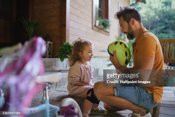 mature man preparing his daughter for first bike ride outdoors in front yard. - cycling helmet stock pictures, royalty-free photos & images