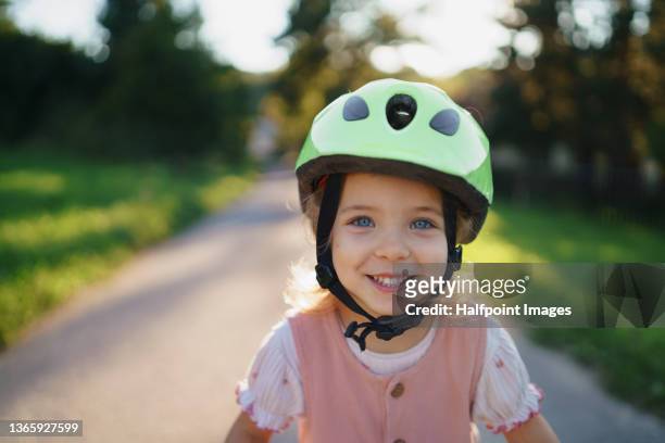 close-up of happy little girl riding a bicycle and looking at camera outdoors in village in summer day. - girl bike stock pictures, royalty-free photos & images