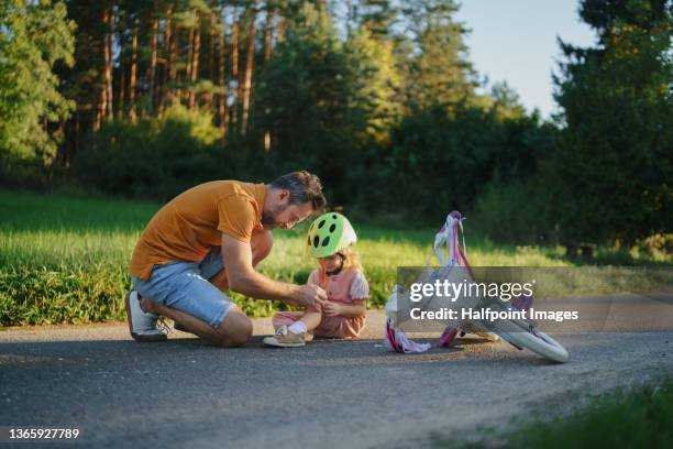 mature man applying bandage to his little daughter after fall from bike outdoors in park. - bicycle crash stock pictures, royalty-free photos & images