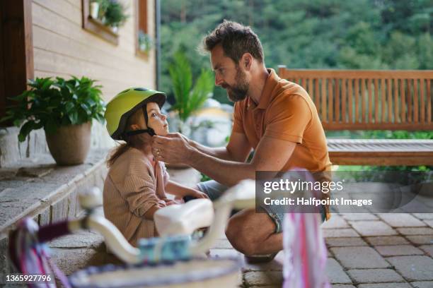 mature man preparing his daughter for first bike ride outdoors in front yard. - protection helmet stock-fotos und bilder