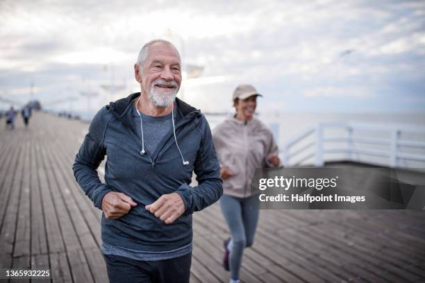 active senior couple runners jogging outdoors on pier by sea in early morning. - endurance stock pictures, royalty-free photos & images