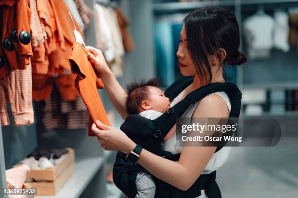 young asian mother shopping for baby clothing with her baby in department store - textile industry uk stock pictures, royalty-free photos & images