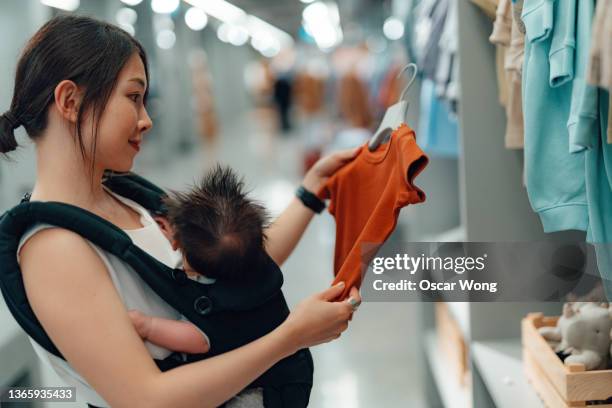 young asian mother shopping for baby clothing with her baby in department store - baby boutique stock pictures, royalty-free photos & images