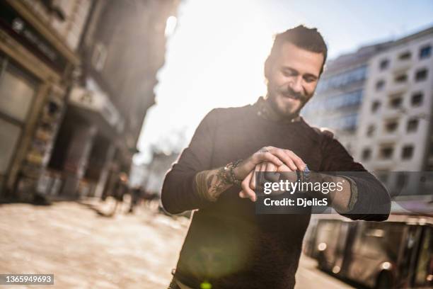 happy young man checking time on his watch on city street. - s happy days stockfoto's en -beelden