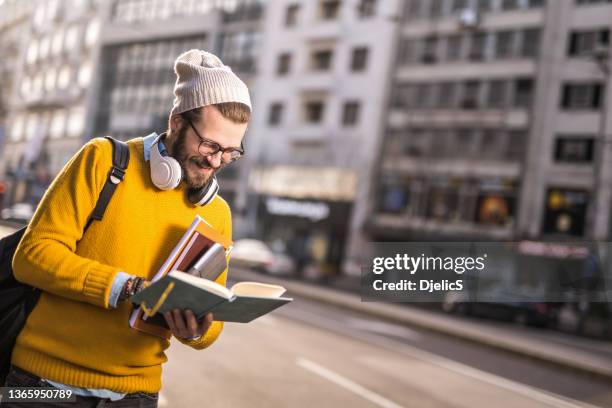 young university student walking on city street and reading. - city book stock pictures, royalty-free photos & images