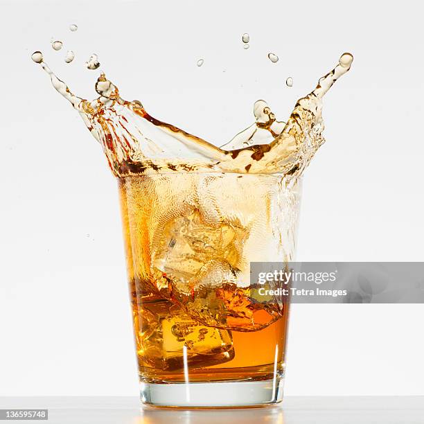 studio shot of ice cubes splashing into glass of whiskey - splashing cocktail stock pictures, royalty-free photos & images