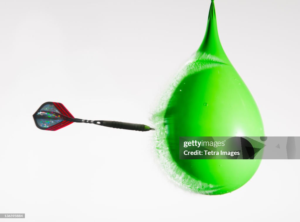 Studio shot of dart puncturing water-filled balloon