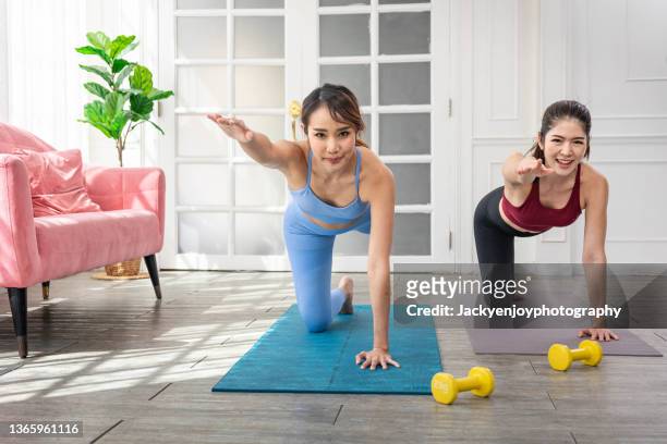 smiling woman and friend practicing yoga on mat in living room at home - day of yoga in bangkok stock-fotos und bilder