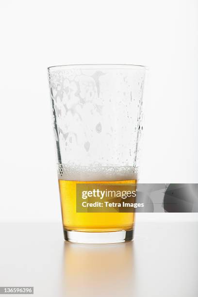 studio shot of half full beer glass - beer glass stock-fotos und bilder