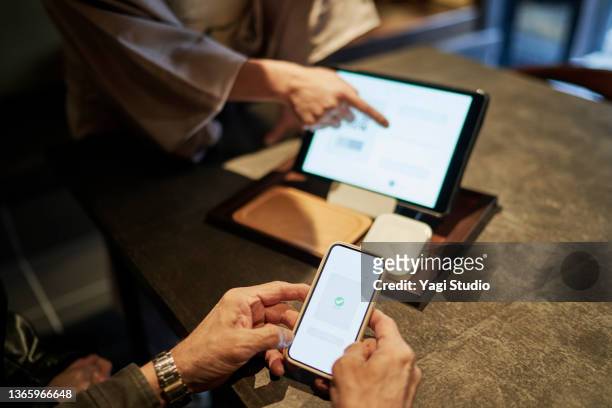 hispanic couple using smart phone to pay while checking into hotel in kyoto, japan - couple travel tablet stock-fotos und bilder