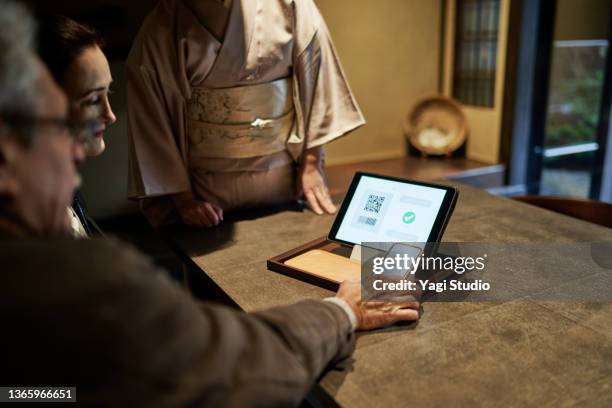 hispanic couple using smart phone to pay while checking into hotel in kyoto, japan - premium access image only stock pictures, royalty-free photos & images