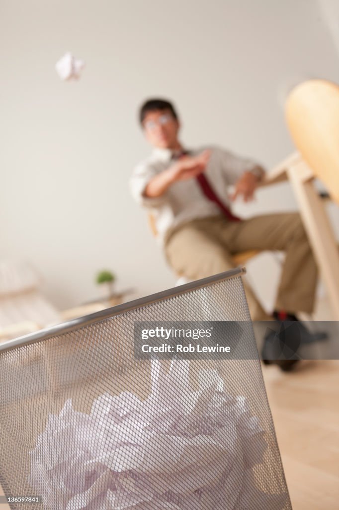 Businessman tossing ball of paper into wastebasket