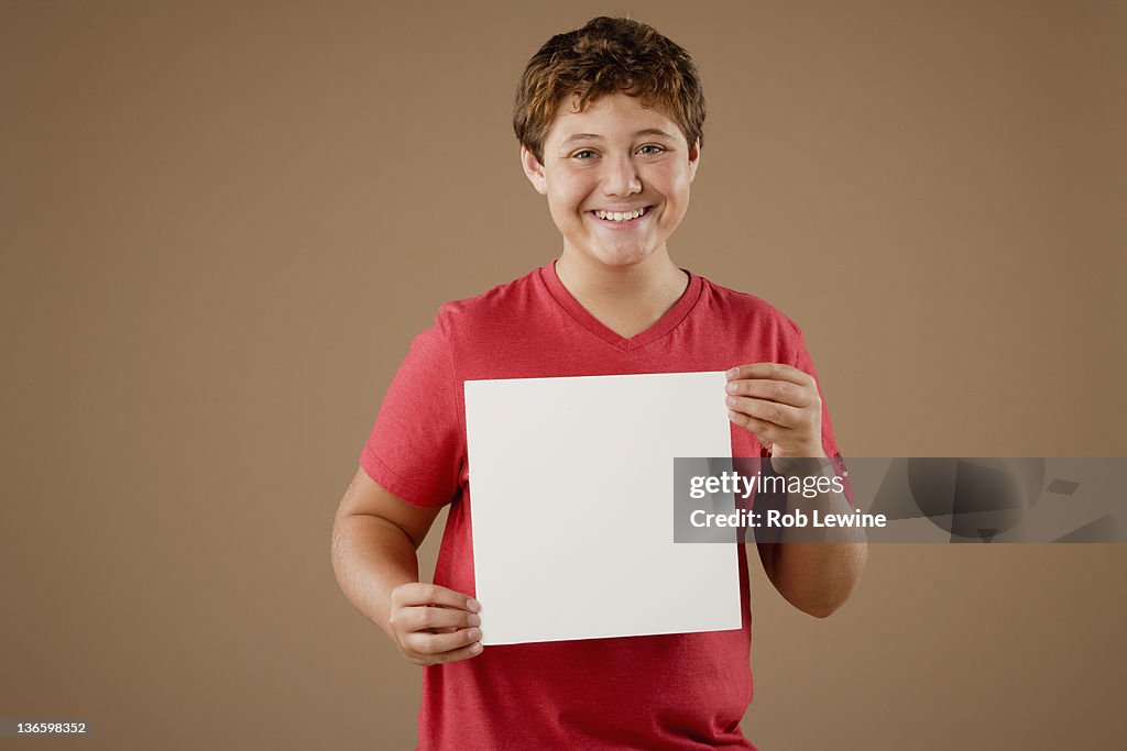 Studio portrait of boy (12-13) holding blank sheet of paper