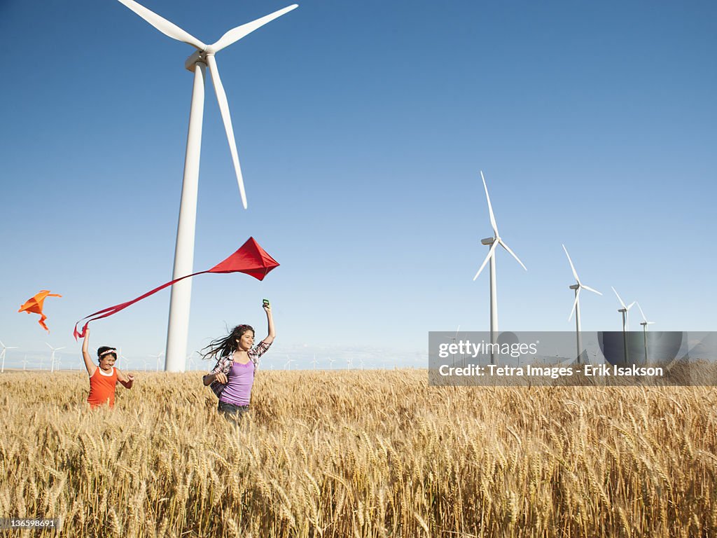 USA, Oregon, Wasco, Girls (10-11, 12-13) playing with kite in wheat field, wind turbines in background