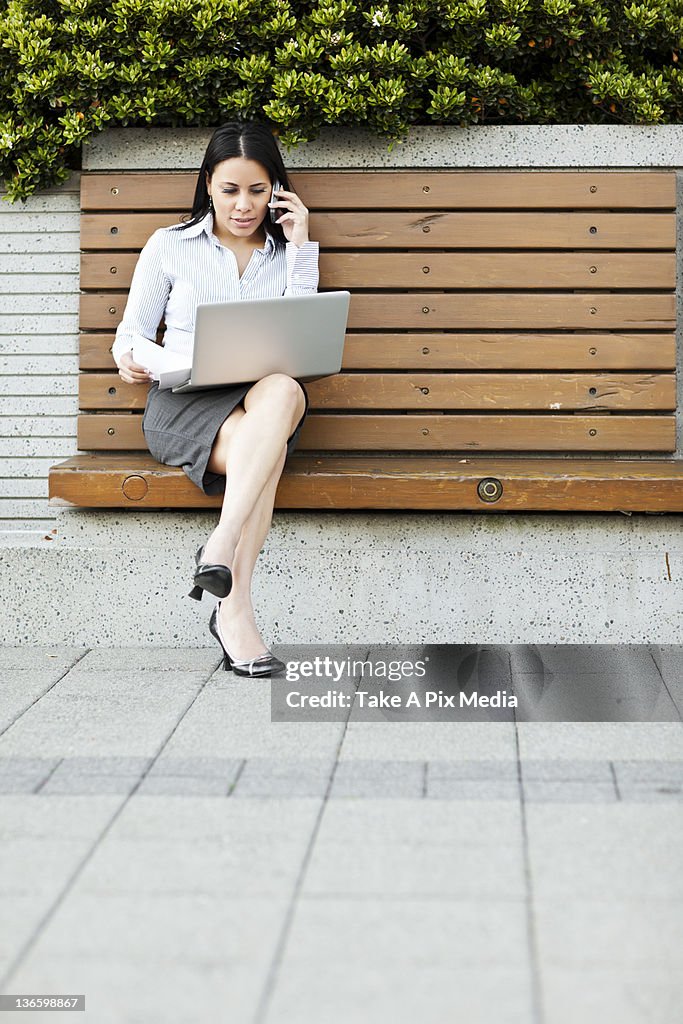 USA, Washington, Seattle, Young businesswoman sitting on bench using laptop