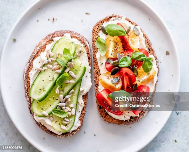 two slices of toast with cream cheese, cucumber, tomato, pumpkin seeds, sesame seeds and basil - schmierkäse stock-fotos und bilder