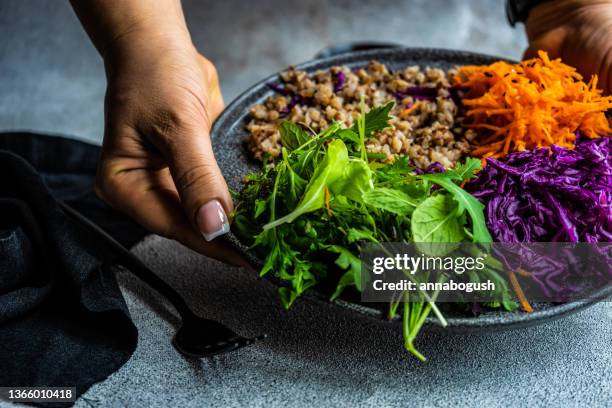 woman holding a plate with buckwheat, carrot, red cabbage and rocket - buckwheat stockfoto's en -beelden