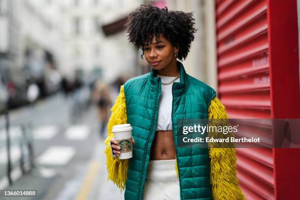 Guest wears gold large earrings, a gold large chain necklace, a white cropped t-shirt with yellow large fluffy fringes long sleeves, a dark green...