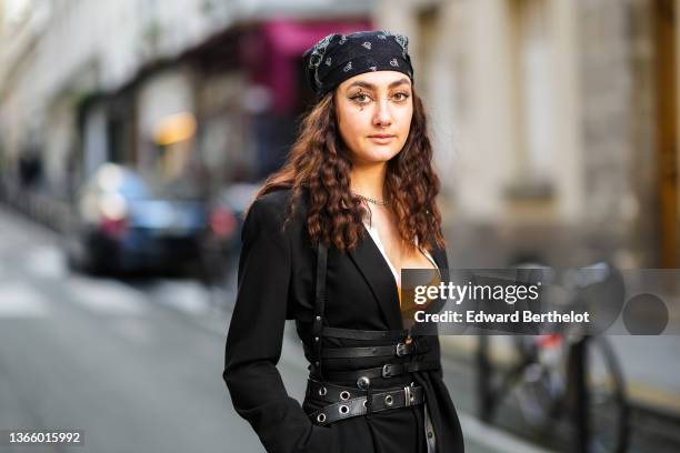 Guest wears a black with white print pattern scarf as a head band, a silver piercing, a silver chain necklace, a white long shirt, an orange V-neck...