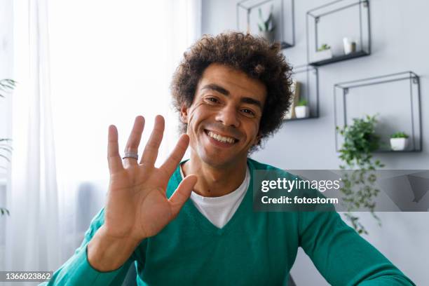 young man waving at camera as if he is on a video call - teal portrait stockfoto's en -beelden