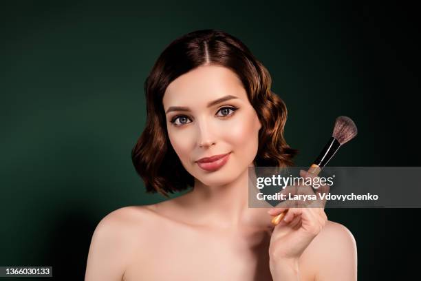 portrait of smiling cool professional makeup artist girl with naked shoulders hold big brush isolated on green color background - big bobs stock pictures, royalty-free photos & images