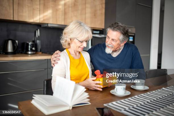 senior man giving a gift to his wife in a home kitchen - luxury lounges stock pictures, royalty-free photos & images