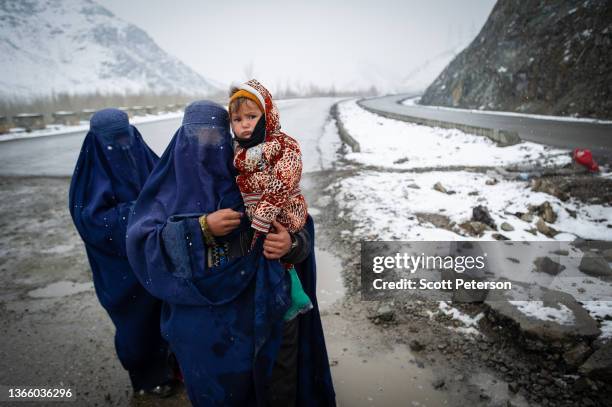 Afghan women beg in the snow, with a child, on the Kabul road south to Pul-e Alam, Afghanistan, on January 17, 2022. The UN World Food Program warns...