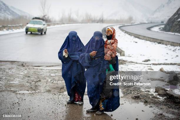 Afghan women beg in the snow, with a child, on the Kabul road south to Pul-e Alam, Afghanistan, on January 17, 2022. The UN World Food Program warns...