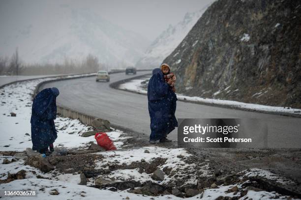 Afghan women beg in the snow, with a child, on the Kabul road south to Pul-e Alam, Afghanistan, on January 17, 2022. The UN World Food Program warns...