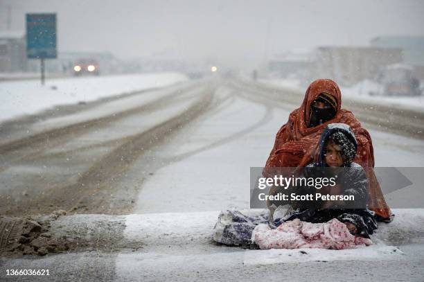 An Afghan woman begs for money from passing cars in the snow, with a child huddled beside her, on the Kabul road south to Pul-e Alam, Afghanistan, on...