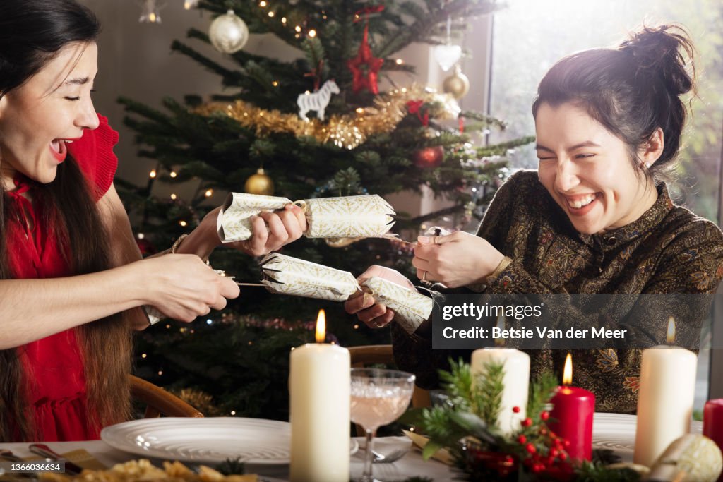 Friends pulling Christmas crackers at dinner table.