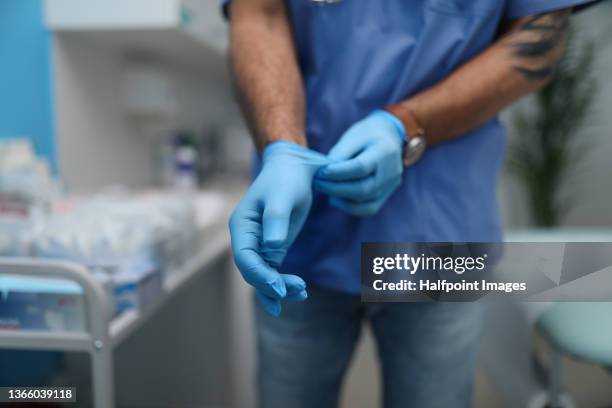 unrecognizable male doctor putting on surgical gloves indoors in hospital. - glove stockfoto's en -beelden