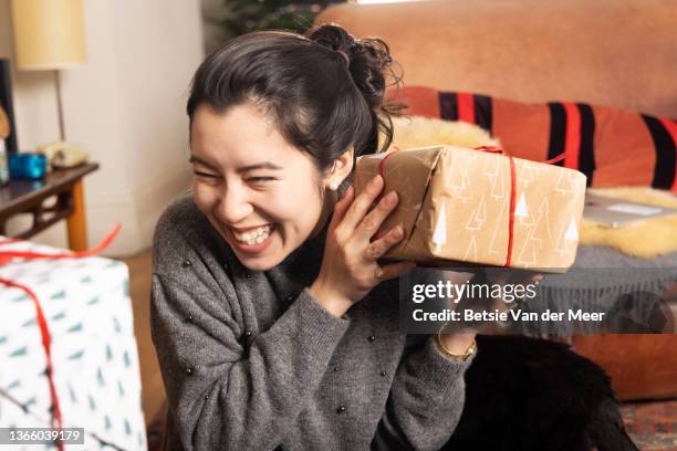 woman shakes present to guess what is inside. - receiving present stock pictures, royalty-free photos & images