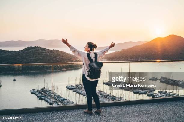 happy woman traveler enjoys views of marina port at sunset - bilsport stockfoto's en -beelden