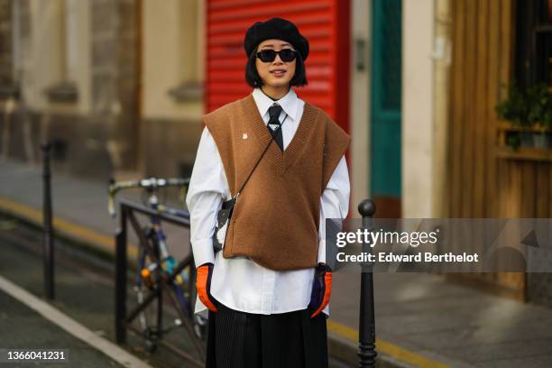 Guest wears a black felt wool beret, sunglasses, a white oversized shirt, a black tie from Prada, a brown wool V-neck sleeveless / shoulder pads...