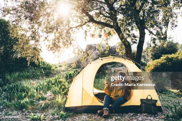 woman hiker uses phone sitting in tent in tourist camp - sheltering stock pictures, royalty-free photos & images