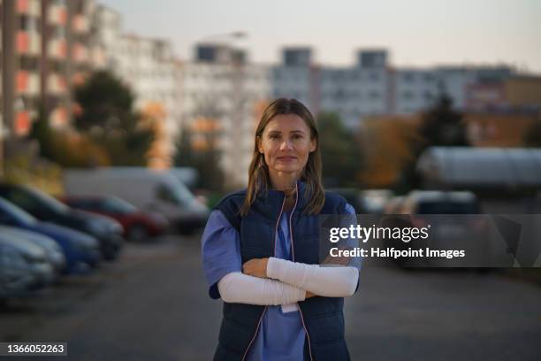 mature female caregiver standing with arms crossed and looking at camera outdoors in town. - doctor with arms crossed stock pictures, royalty-free photos & images