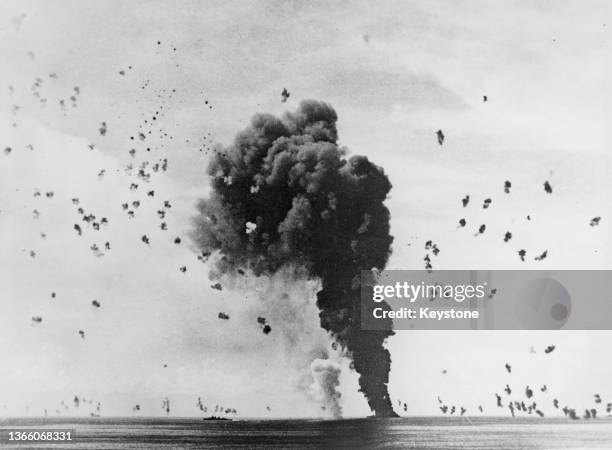 The United States Navy Fletcher Class Destroyer USS Claxton puts up covering anti aircraft fire as oil smoke rises from the burning and sinking USS...