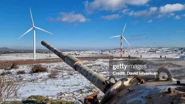 The turret of an abandoned Israeli army tank, left in place after the 1973 Yom Kippur War, points towards Syria and a pair of wind turbines from the...