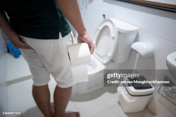 man holding toilet tissue roll in bathroom looking at loo - urinating stock-fotos und bilder