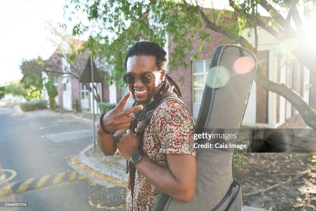 Portrait happy male musician with guitar case gesturing peace sign