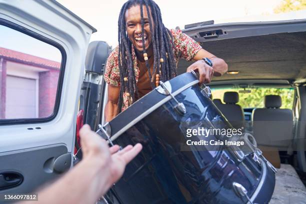 happy male musician loading drum into van - musician male energy stock-fotos und bilder