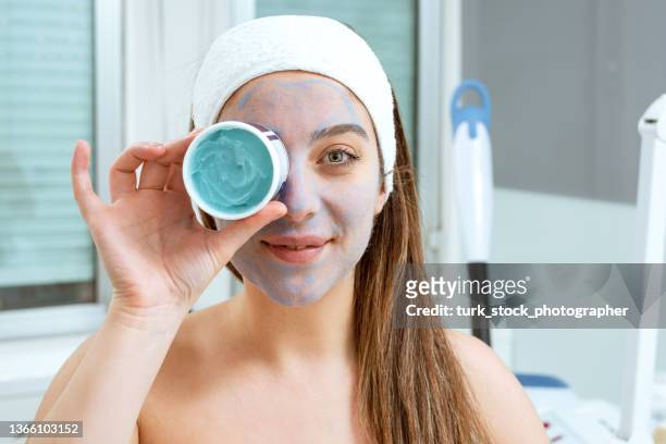 smiling happy woman with exfoliating mask at beauty spa holding mask container on her eye - dry skin stock pictures, royalty-free photos & images