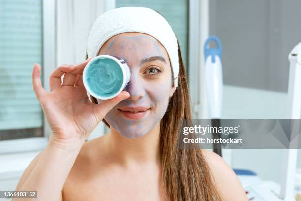 mulher feliz sorridente com máscara esfoliante em spa de beleza segurando recipiente de máscara em seu olho - face mask beauty product - fotografias e filmes do acervo