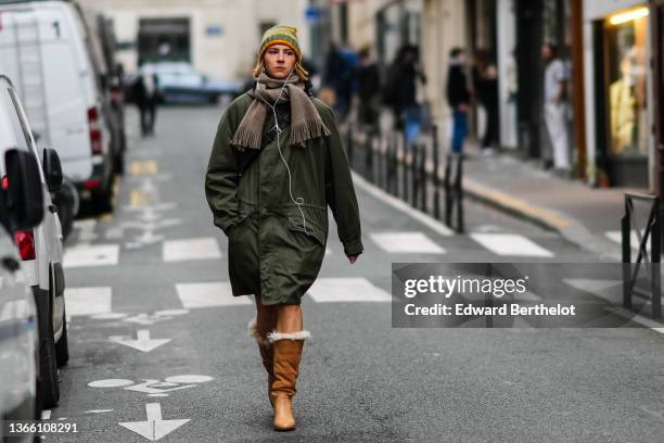 Guest wears a green / yellow / red striped wool beanie, a gray fringed wool scarf, a khaki oversized long puffer jacket, brown leather and suede with...