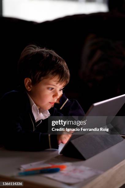 handsome boy in school uniform does homework at home with a tablet - tecnología stock-fotos und bilder