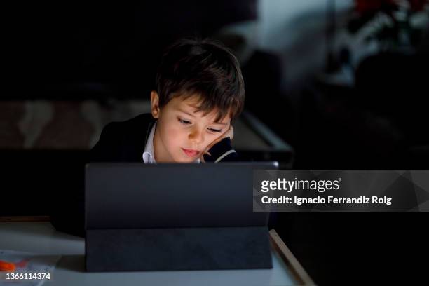 handsome boy in school uniform does homework at home with a tablet - tecnología foto e immagini stock