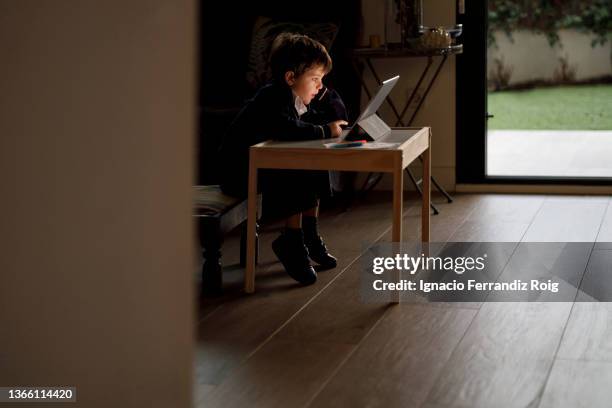 handsome boy in school uniform does homework at home with a tablet - tecnología foto e immagini stock