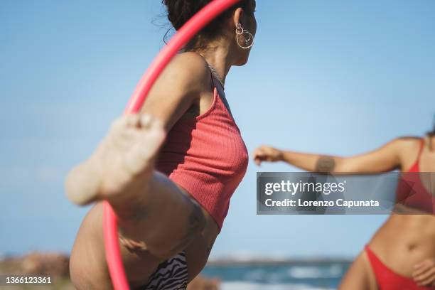 woman spinning plastic hoop while standing on one leg on the beach. - hoop rolling stock pictures, royalty-free photos & images