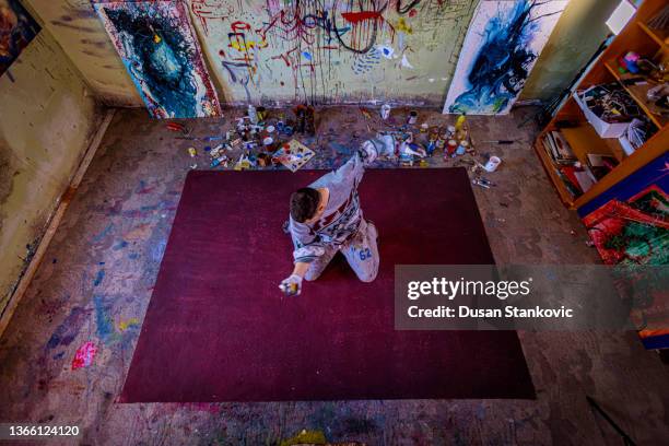 high angle view of male artist splashing the paint on a big red canvas - fine art stock pictures, royalty-free photos & images